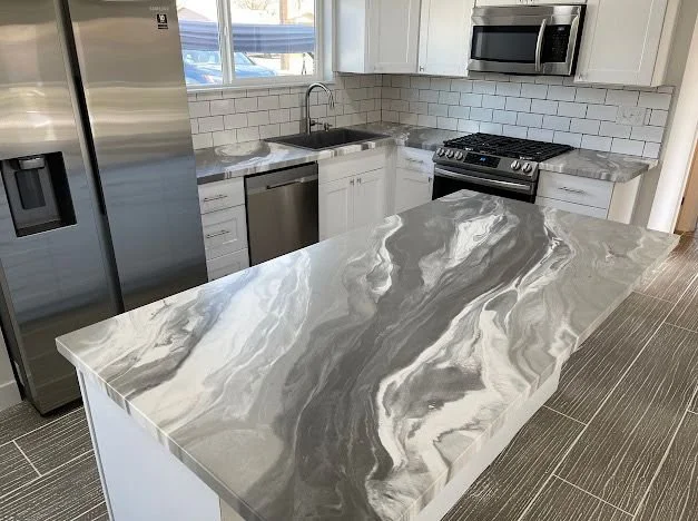 Close-up of a black and blue marble-patterned granite countertop with a black undermount sink and a black faucet in a modern kitchen with white cabinets.