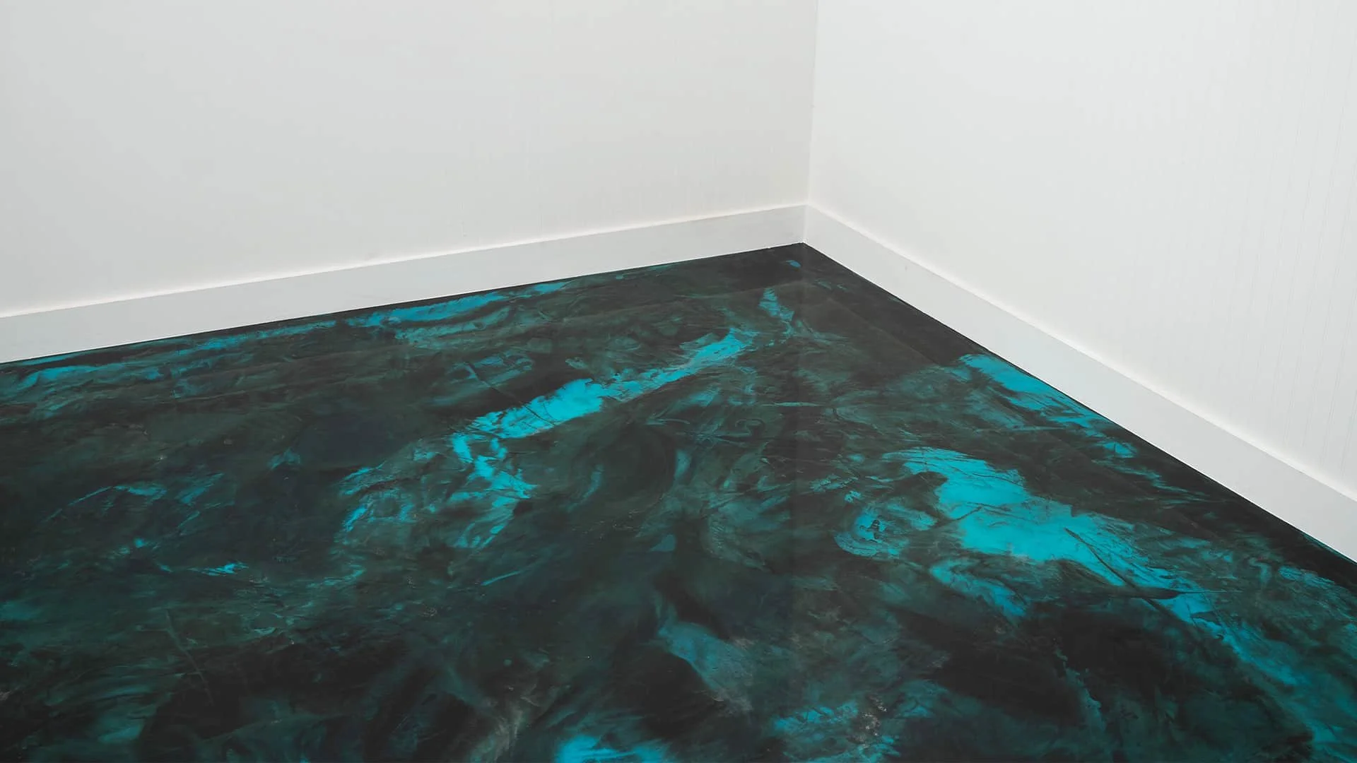 Close-up of a corner in a room with white walls and a dark green and blue marbled floor.
