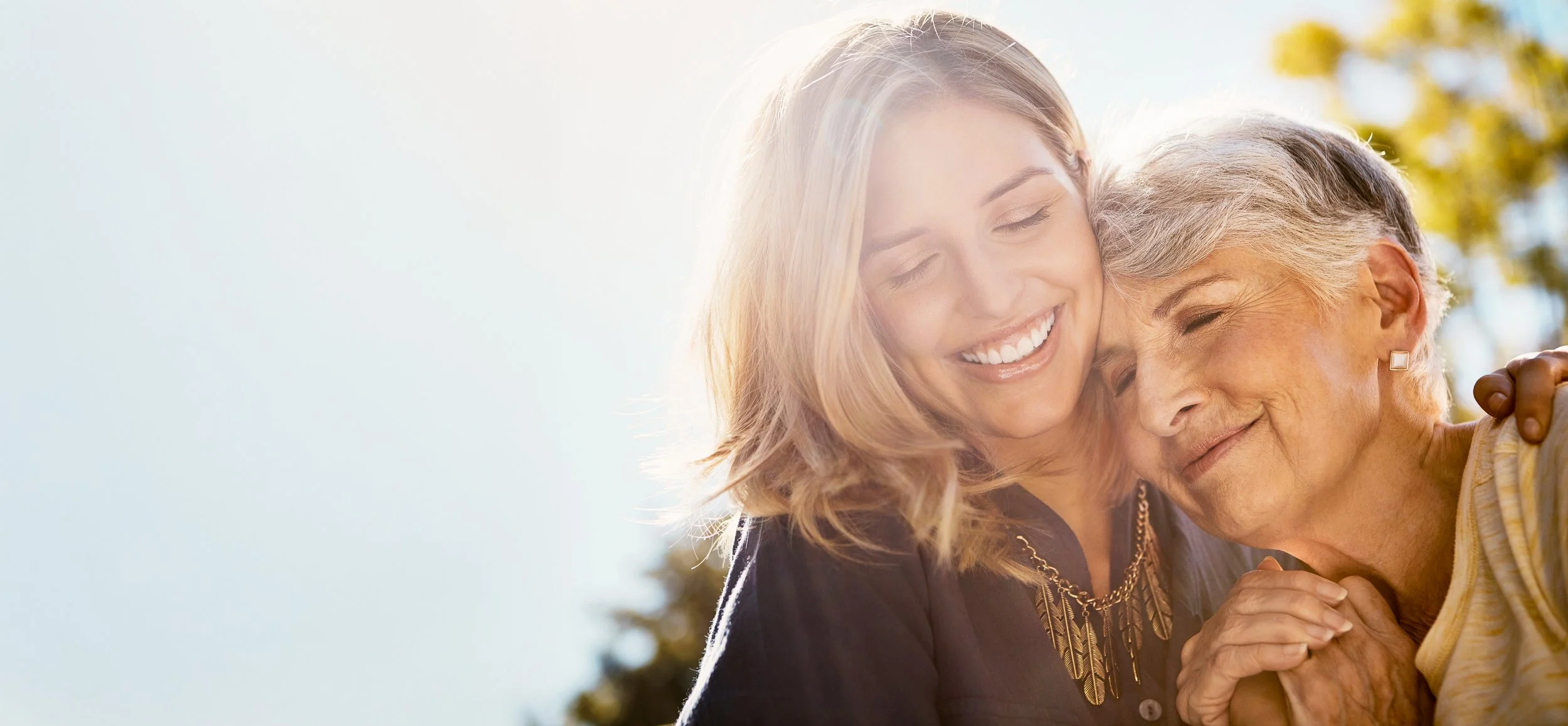 A young woman and an elderly woman share a warm embrace outdoors