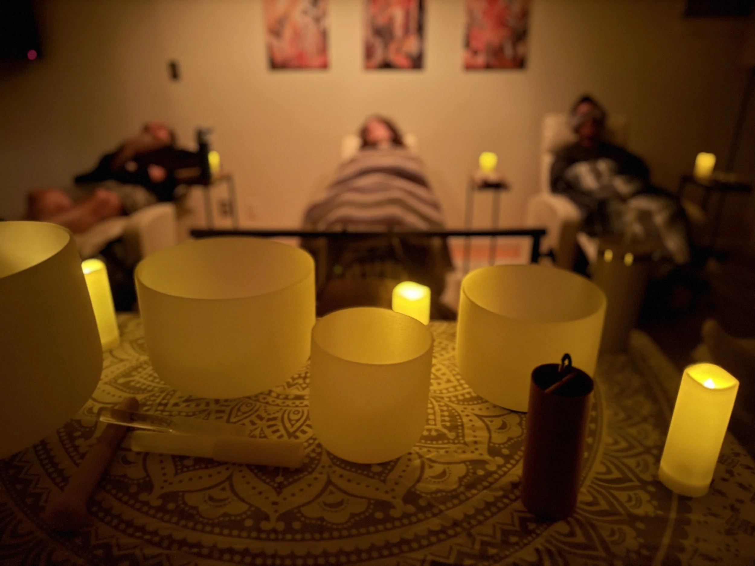 A gathering room with yellow candles on a table, with three people sitting in chairs in the background, blurred.