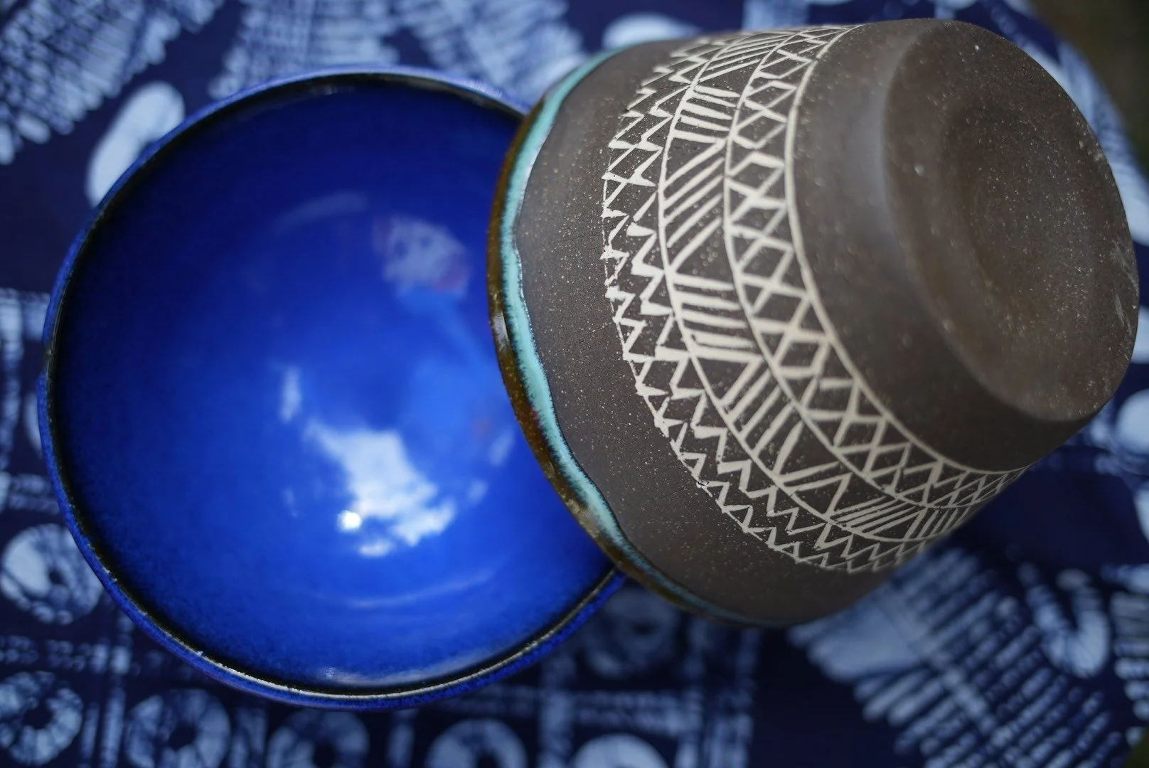 Two dark brown ceramic ice cream bowls atop each other in front of a west african indigo cloth background