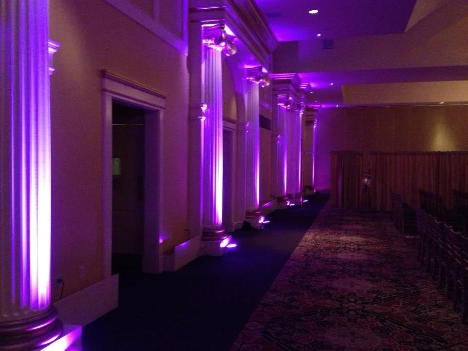 Interior of a banquet hall or event space illuminated with purple uplights on tall columns and ceiling provided by DJ Reece