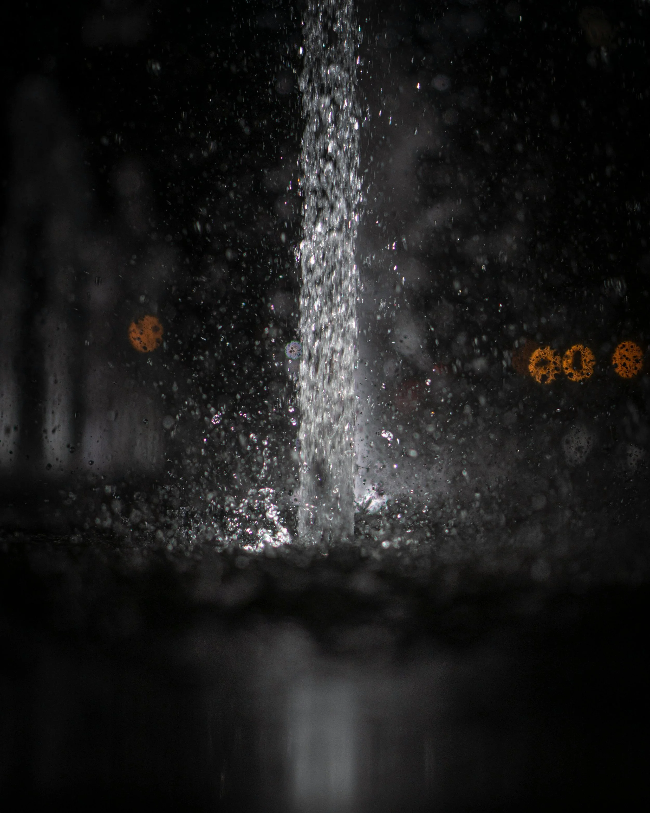 Close-up of water pouring in a dark environment, with blurred lights in the background.