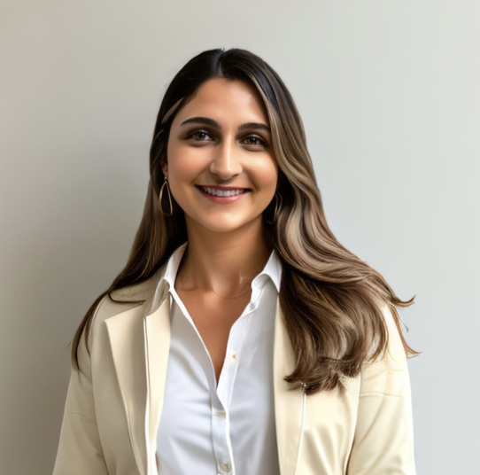 Portrait of a smiling woman with long, wavy brown hair wearing a white blouse and a beige blazer, standing against a plain light-colored background.