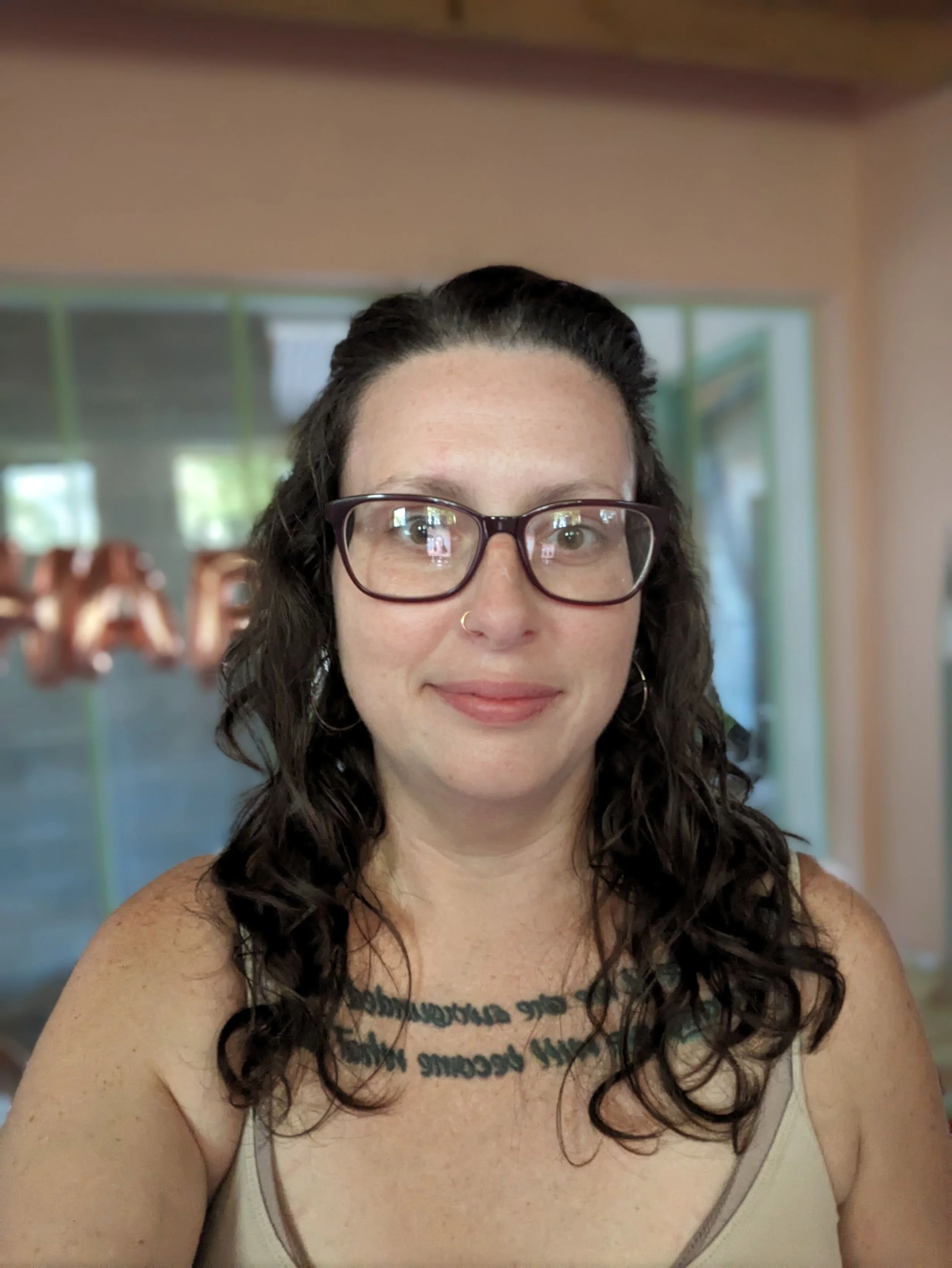 A woman with glasses and brown curly hair smiling indoors.