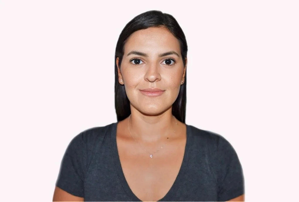 A woman with straight dark hair, wearing a dark gray V-neck shirt, smiling gently, against a plain light background.