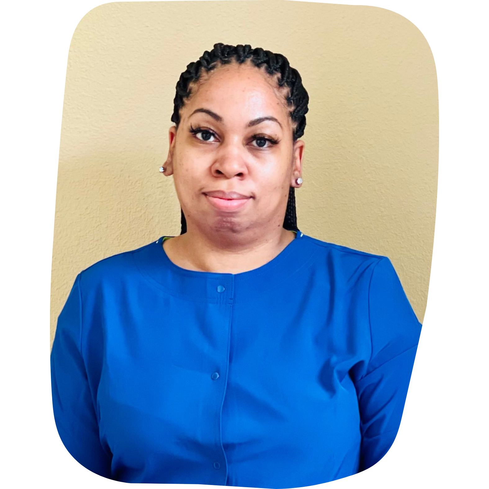 A woman with braided hair and earrings wears a blue top and stands against a beige wall.