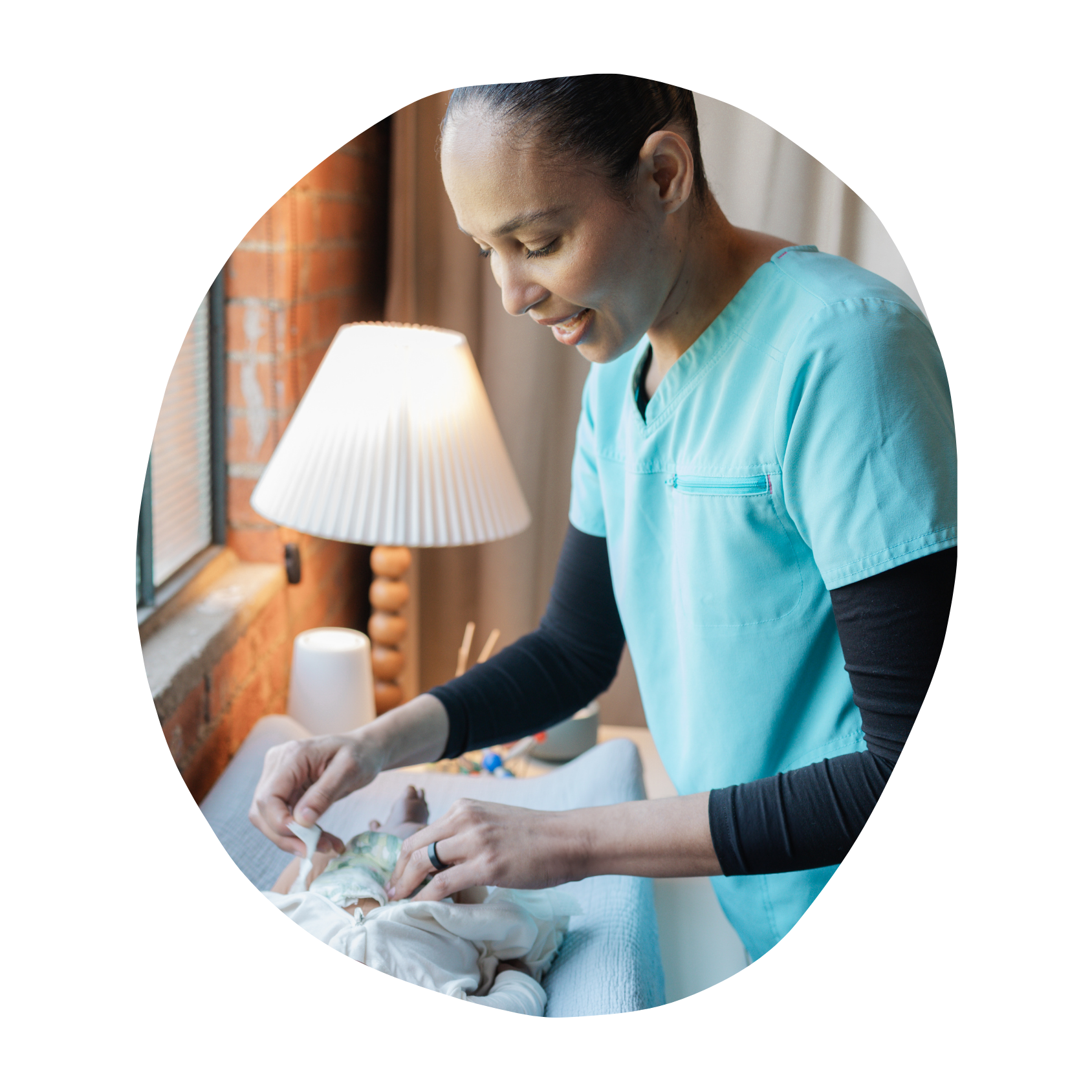 A healthcare worker in scrubs caring for a newborn baby on a changing table in a warmly lit room.