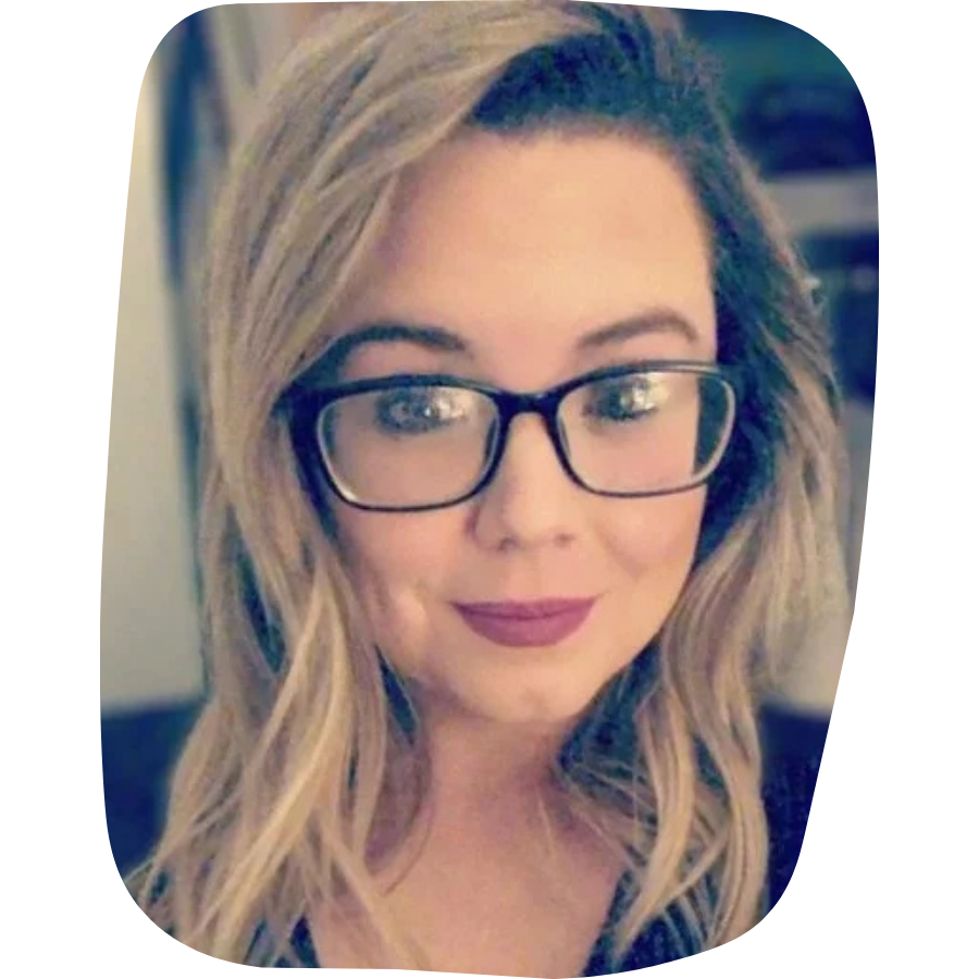 A woman with long wavy blonde hair wearing black glasses and makeup, smiling at the camera.