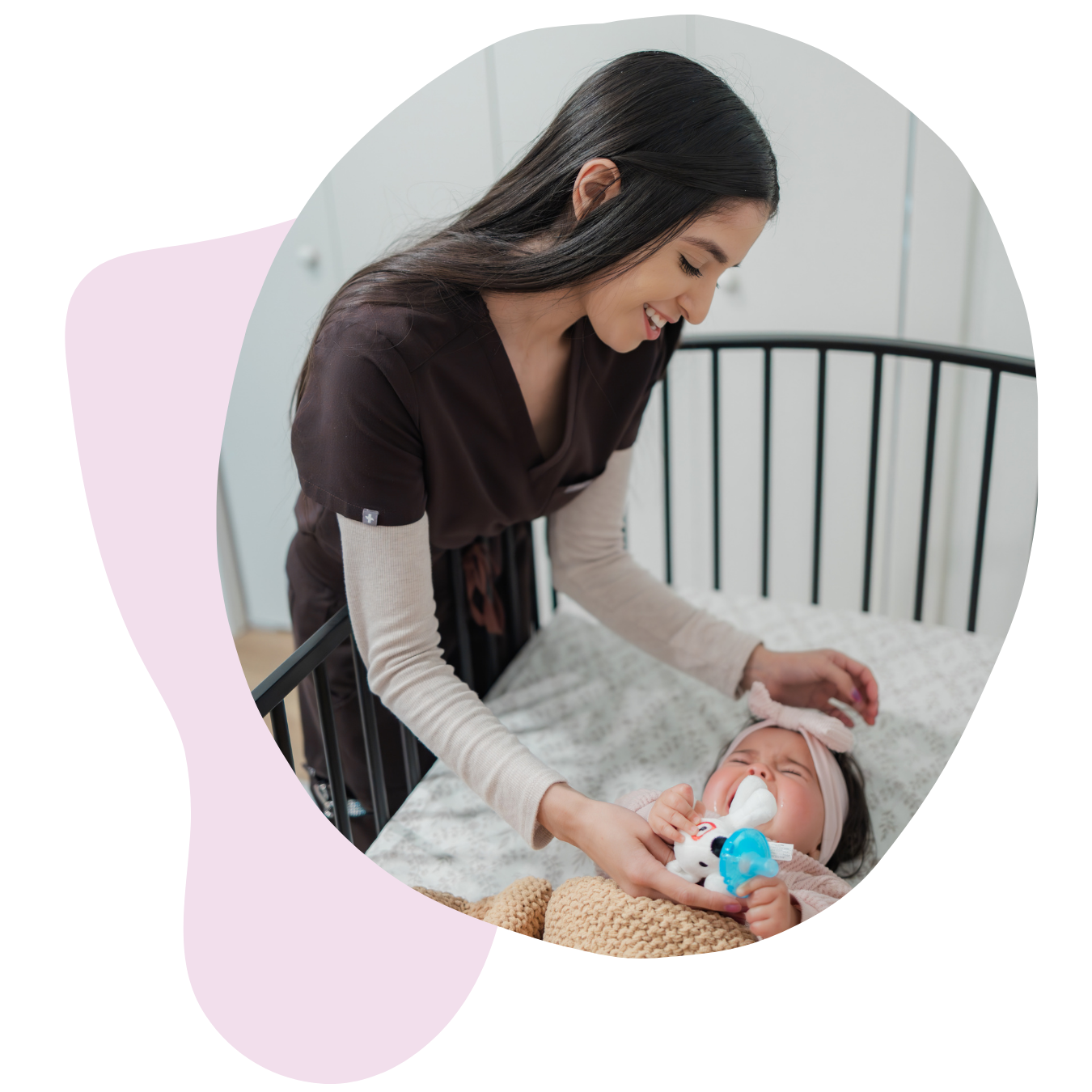 A nurse caring for an infant lying in a crib, holding a pacifier and smiling.