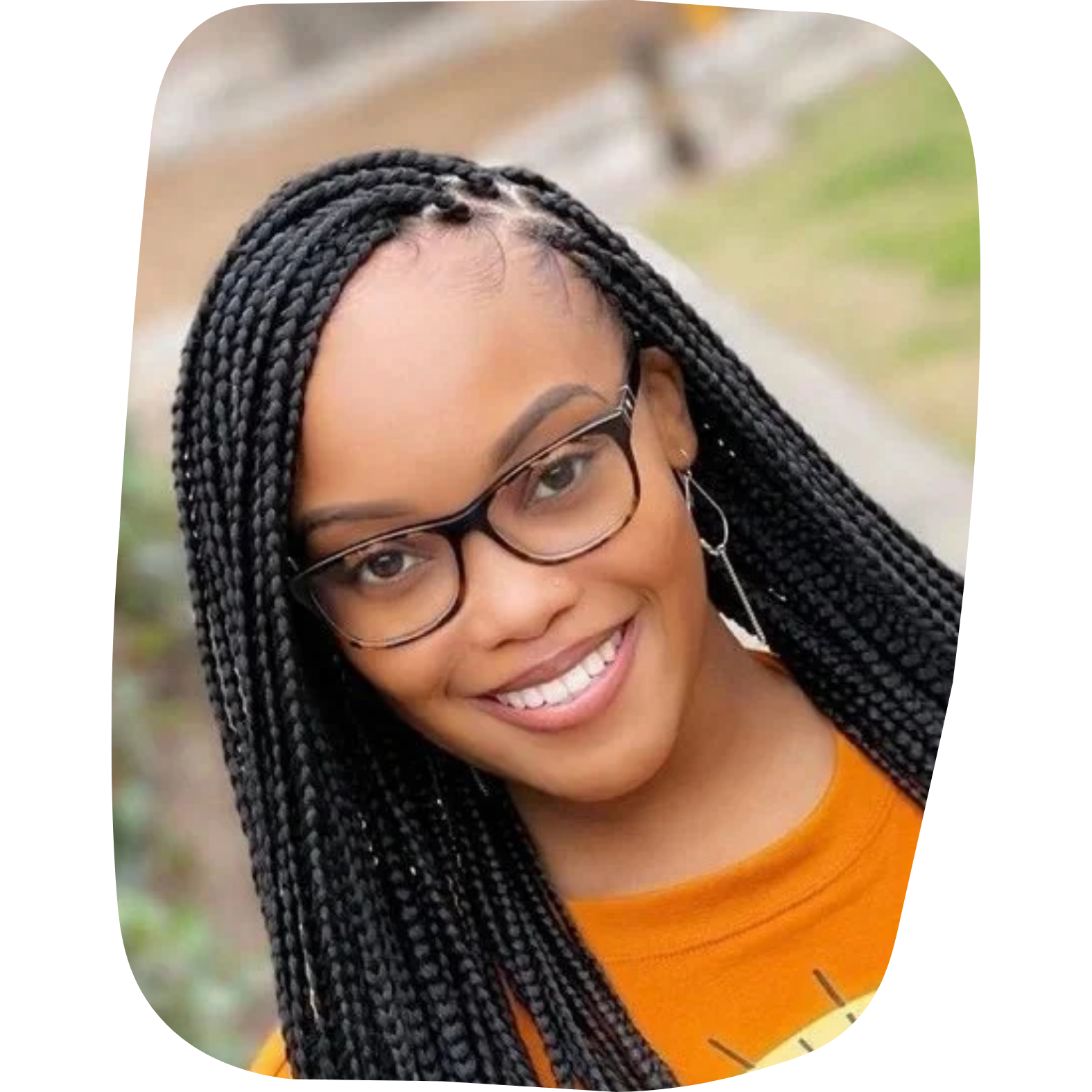 Young woman smiling, wearing glasses, with braided hair, earrings, and an orange shirt, outdoors.