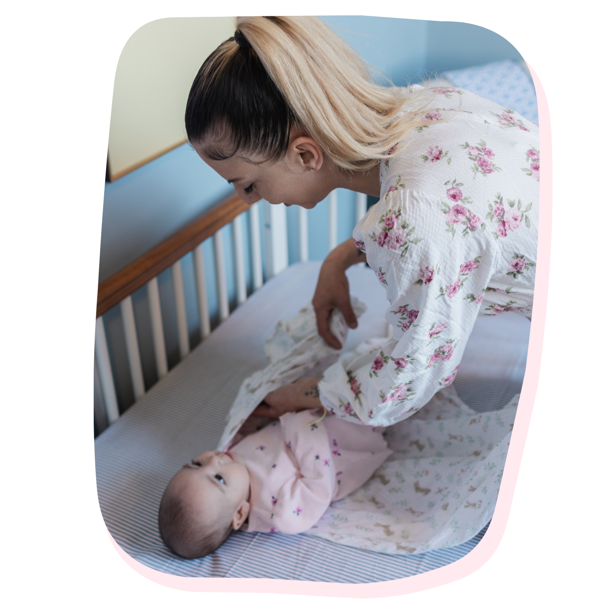 A woman in a floral nightgown adjusting a baby lying on a crib mattress.