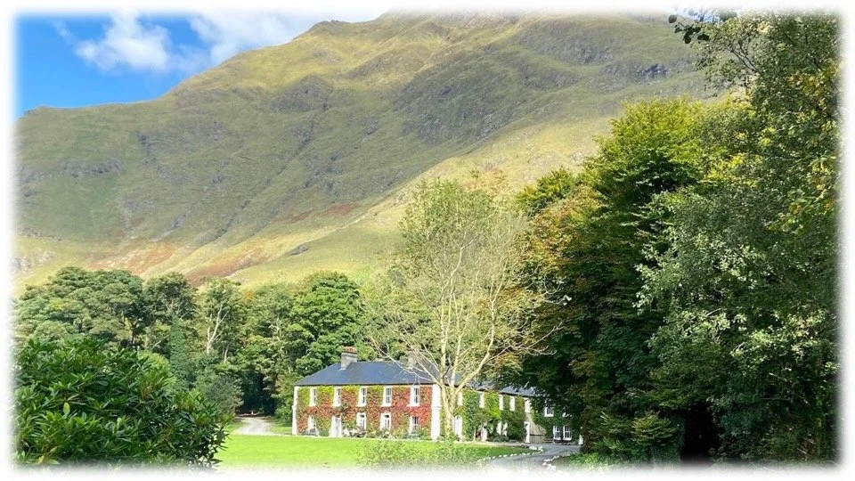 Delphi Lodge, the inspiration for Blackwater Hall from Amanda Geard's "The Midnight House", situated in lush green trees and grass at the foot of a mountain.