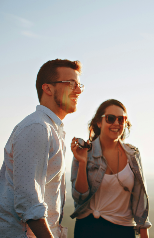 A man and woman outdoors at sunset, smiling and laughing.
