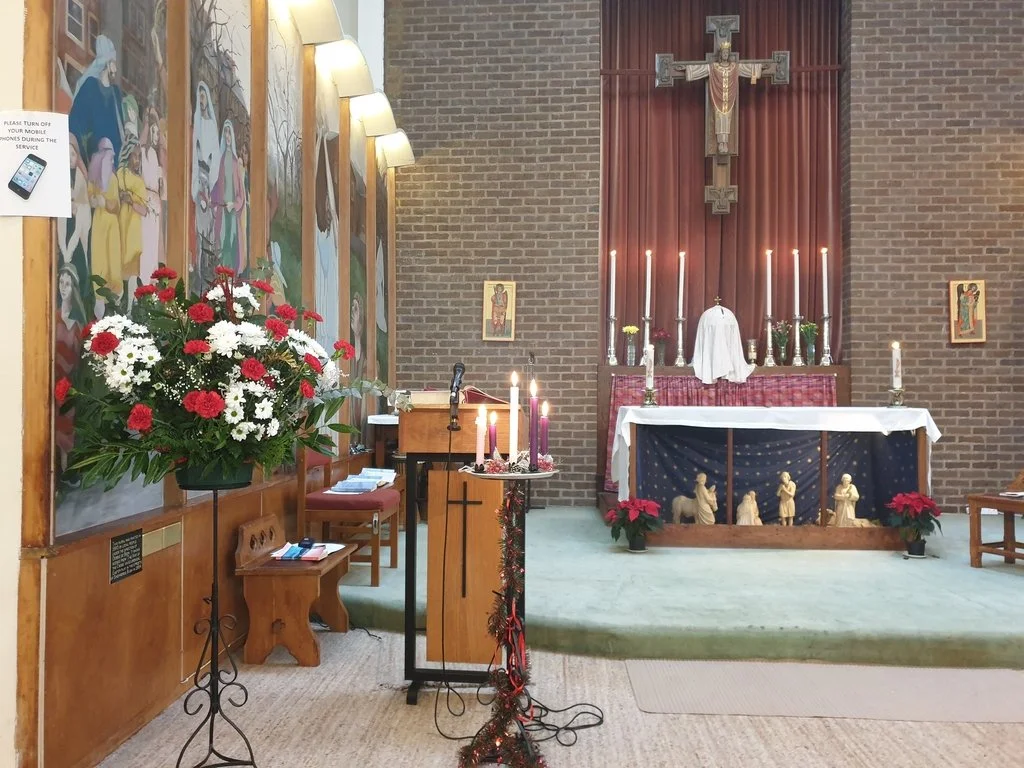 An indoor church altar decorated with poinsettias, candles, and religious icons for Christmas or a church service.