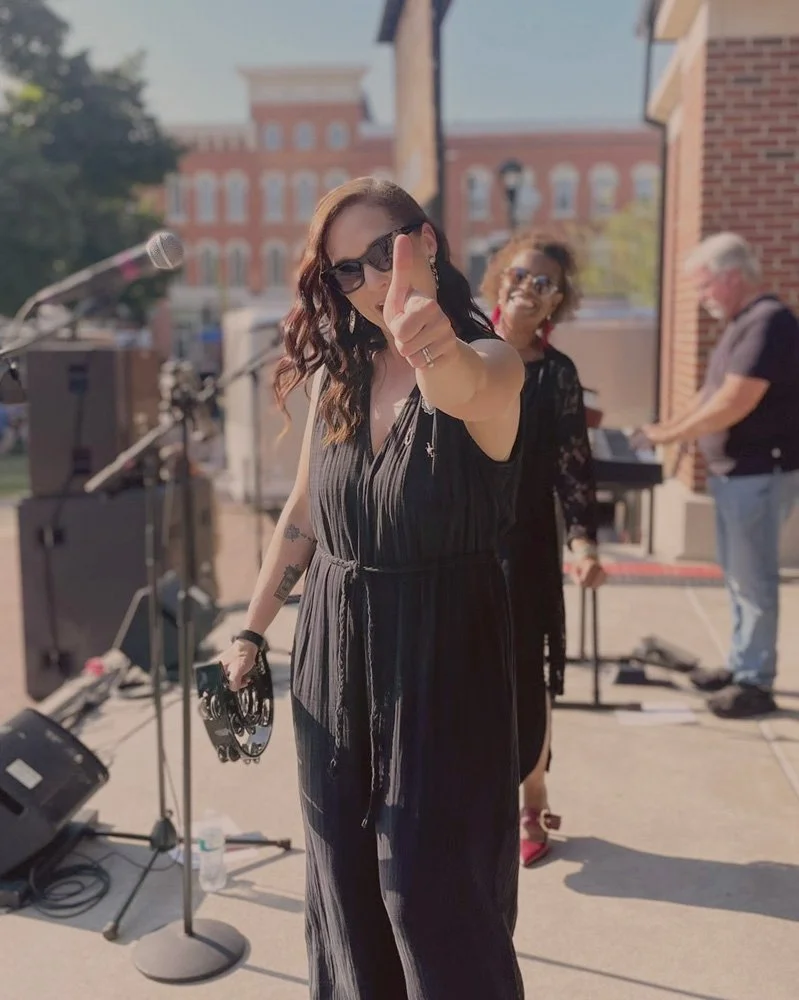 Abigail performing on stage and giving a thumbs-up. Her bandmates stand in the background.