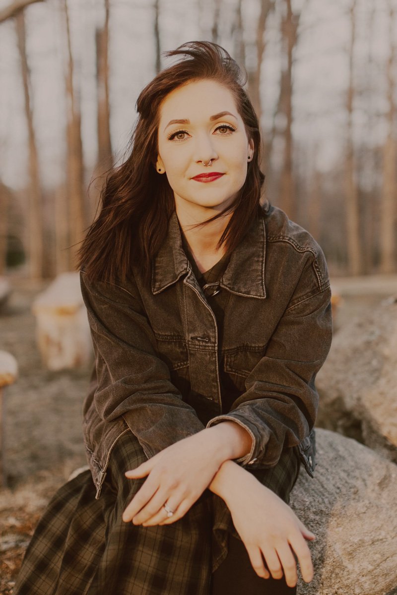 Abigail sits on a rock in a forest and smiles.