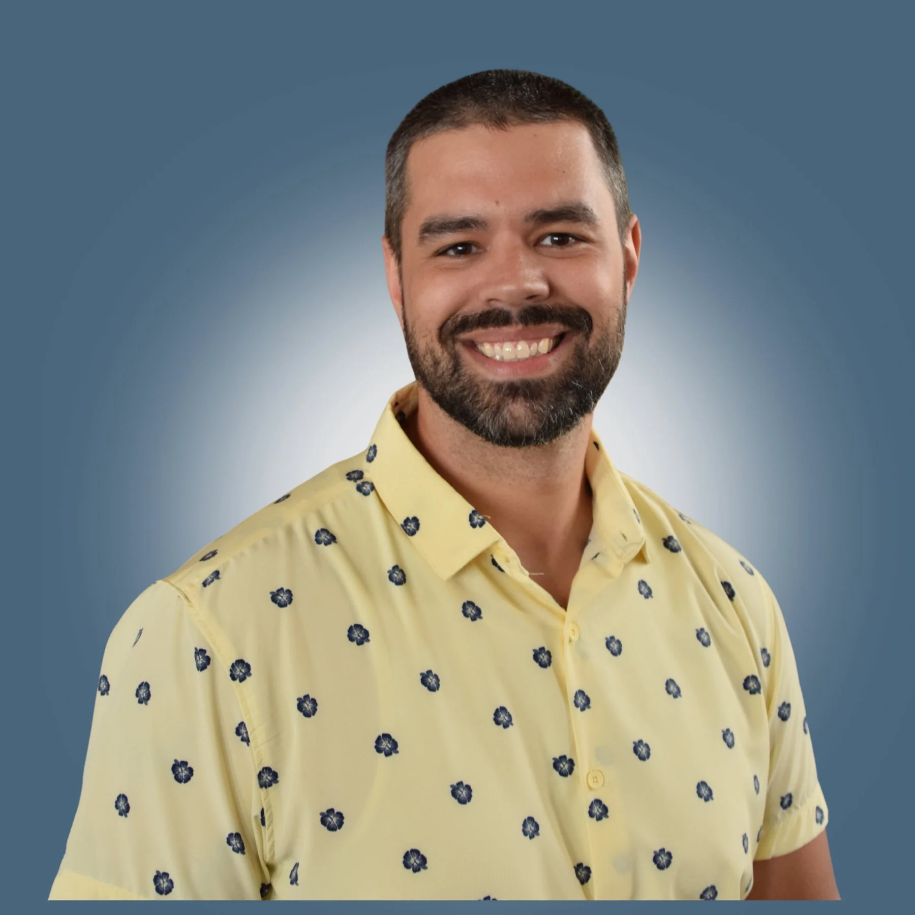 Headshot of a smiling man with a beard, wearing a yellow shirt with a small dark pattern, against a gradient blue background.
