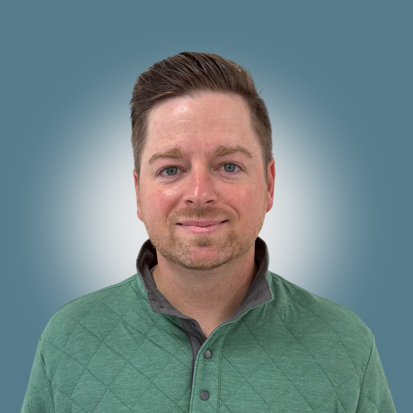 Portrait of a man with short brown hair, blue eyes, light skin, wearing a green quilted polo shirt, against a gradient background.