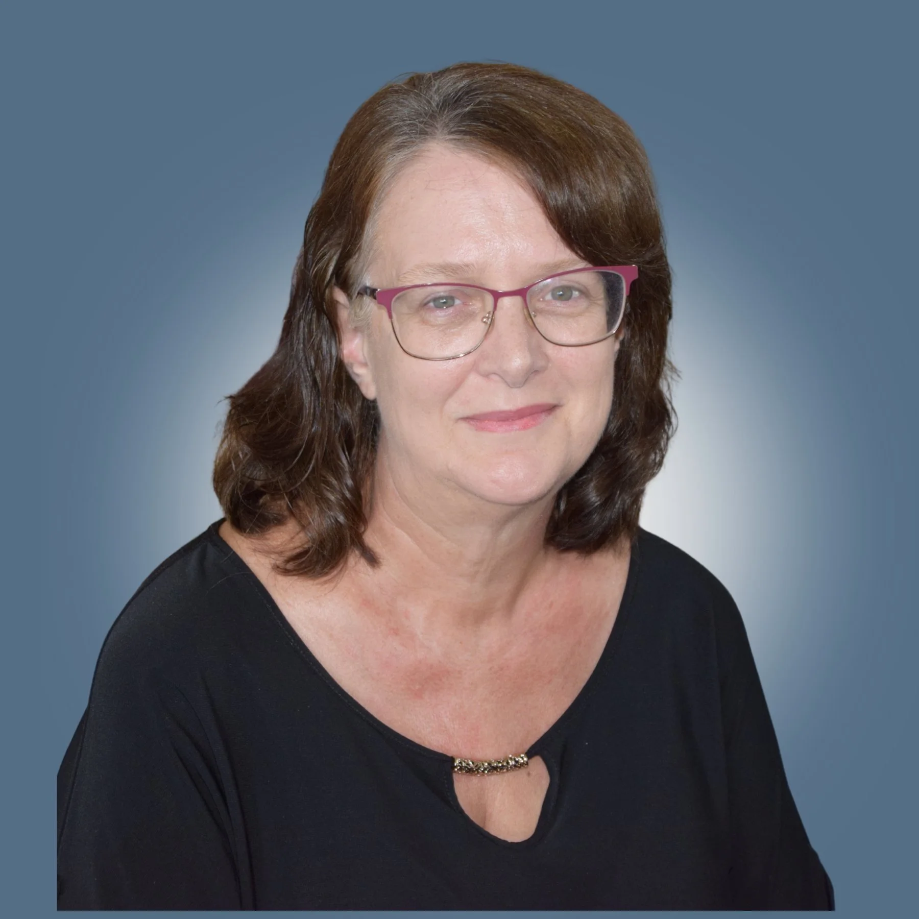 Portrait of a middle-aged woman with glasses and shoulder-length brown hair, wearing a black top, smiling against a plain, dark background.