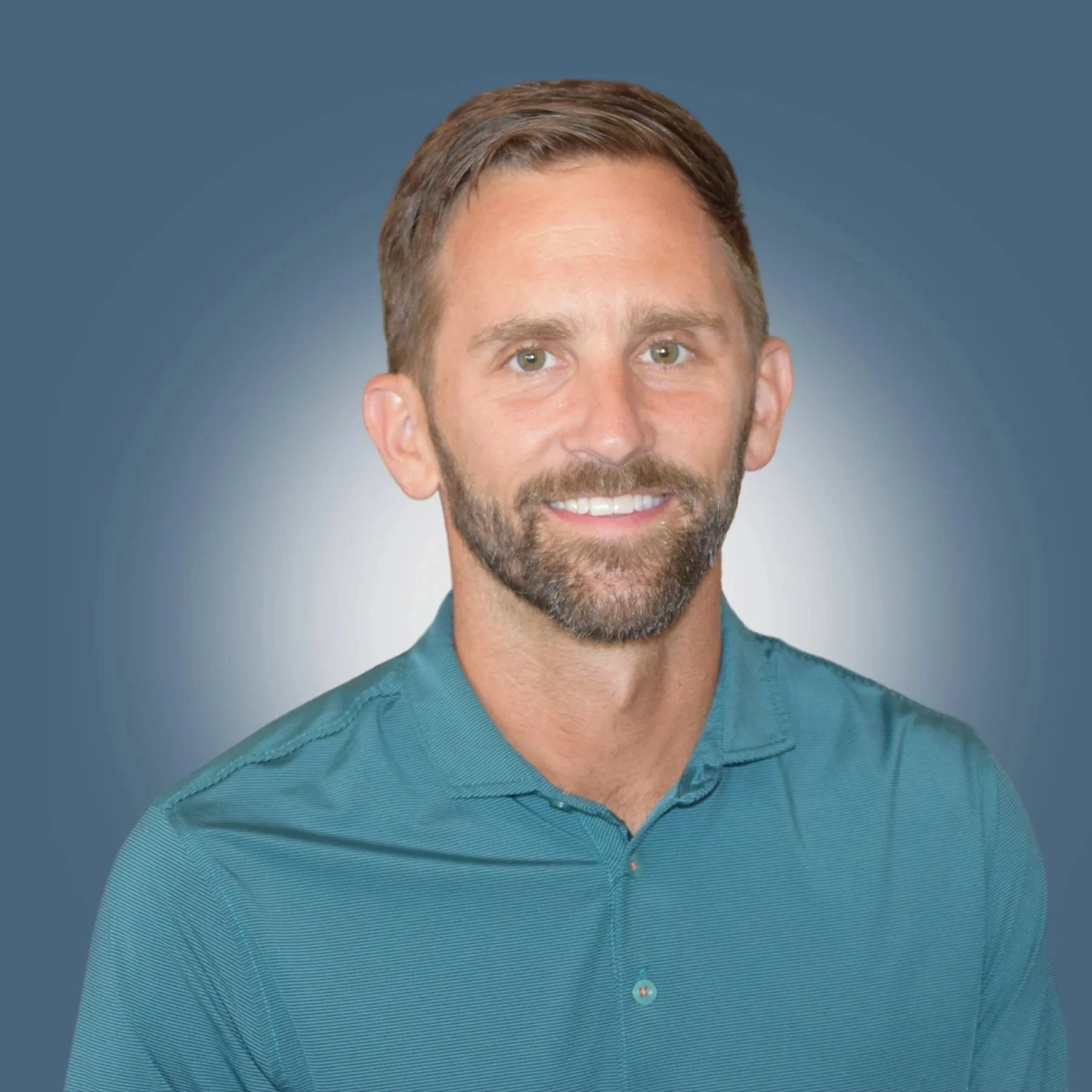 Portrait of a man with short brown hair, beard, and green eyes, wearing a teal button-up shirt, smiling against a blue gradient background.