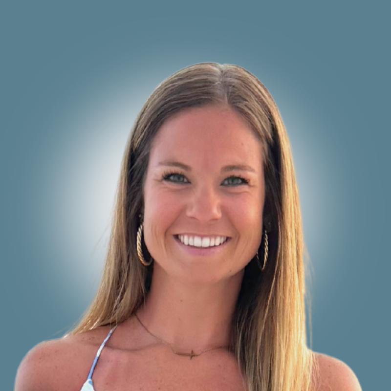 A smiling woman with long brown hair, hoop earrings, wearing a necklace and a light-colored spaghetti strap top, standing against a blue background with a vignette effect.