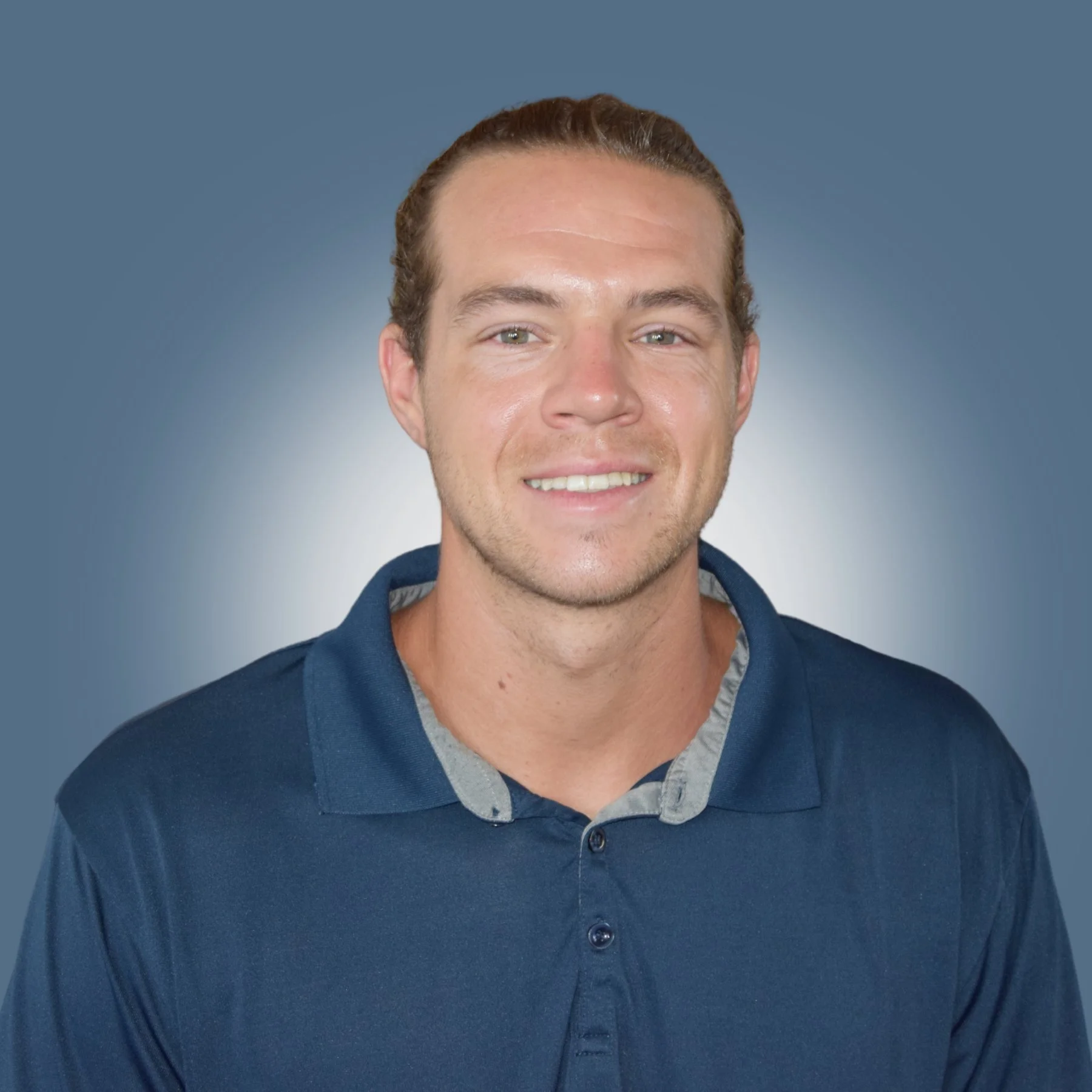 Portrait of a young man smiling, wearing a navy blue polo shirt against a gradient blue background.