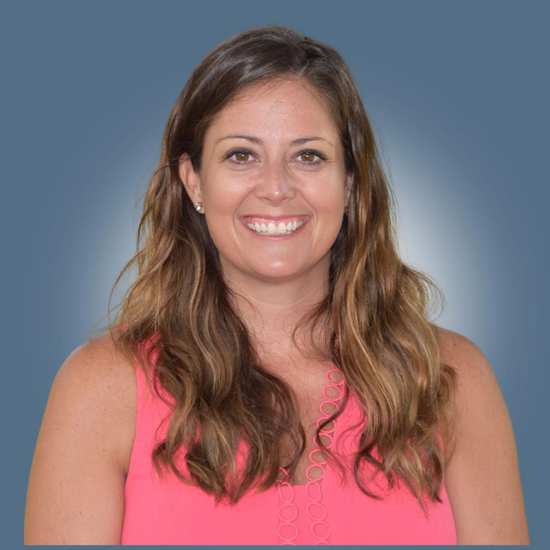 A smiling woman with long brown wavy hair wearing a pink sleeveless top and a pink necklace, against a blue background.