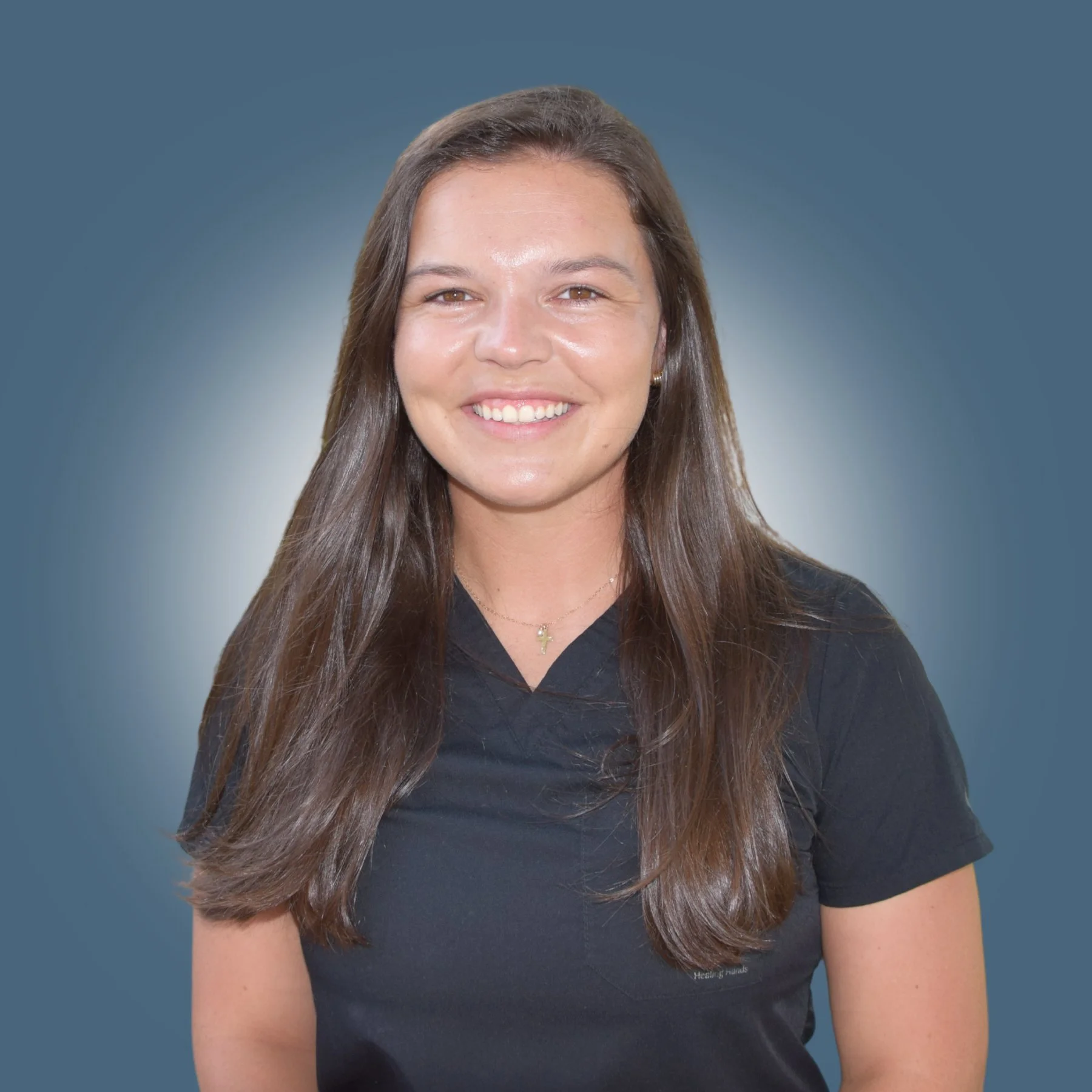 Young woman with long brown hair smiling, wearing a black shirt and a small cross necklace, against a blue background.