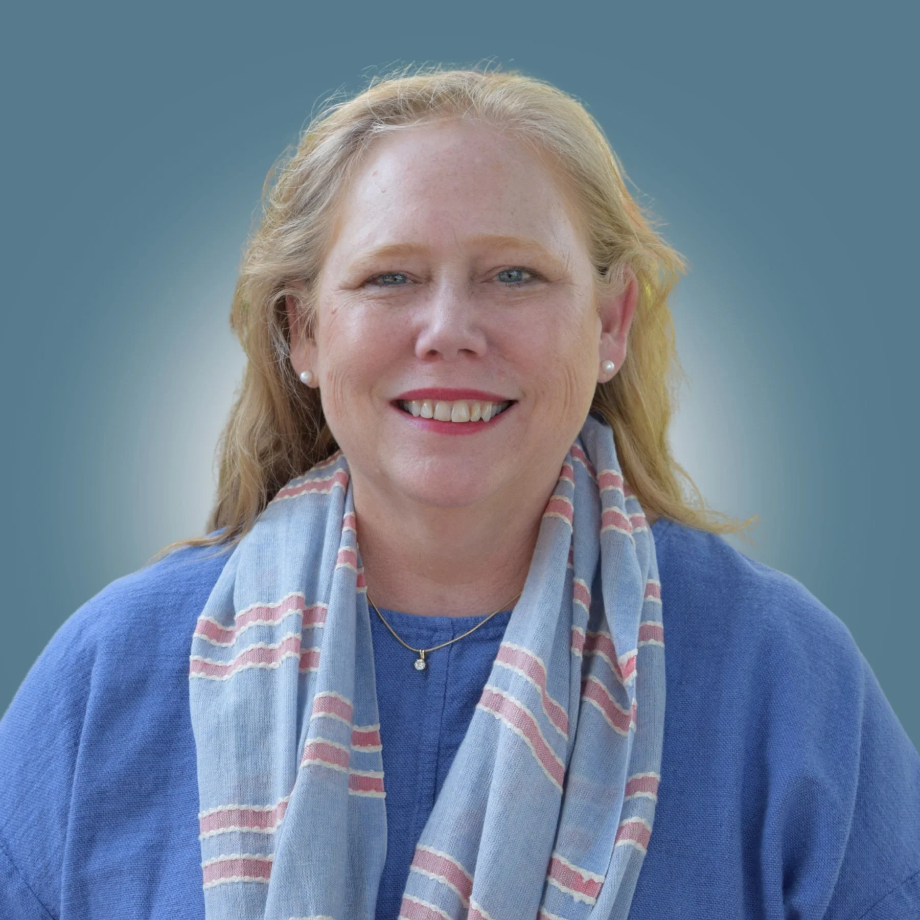 A woman with blonde hair, wearing a blue sweater and a light scarf, smiling against a blurred blue background.