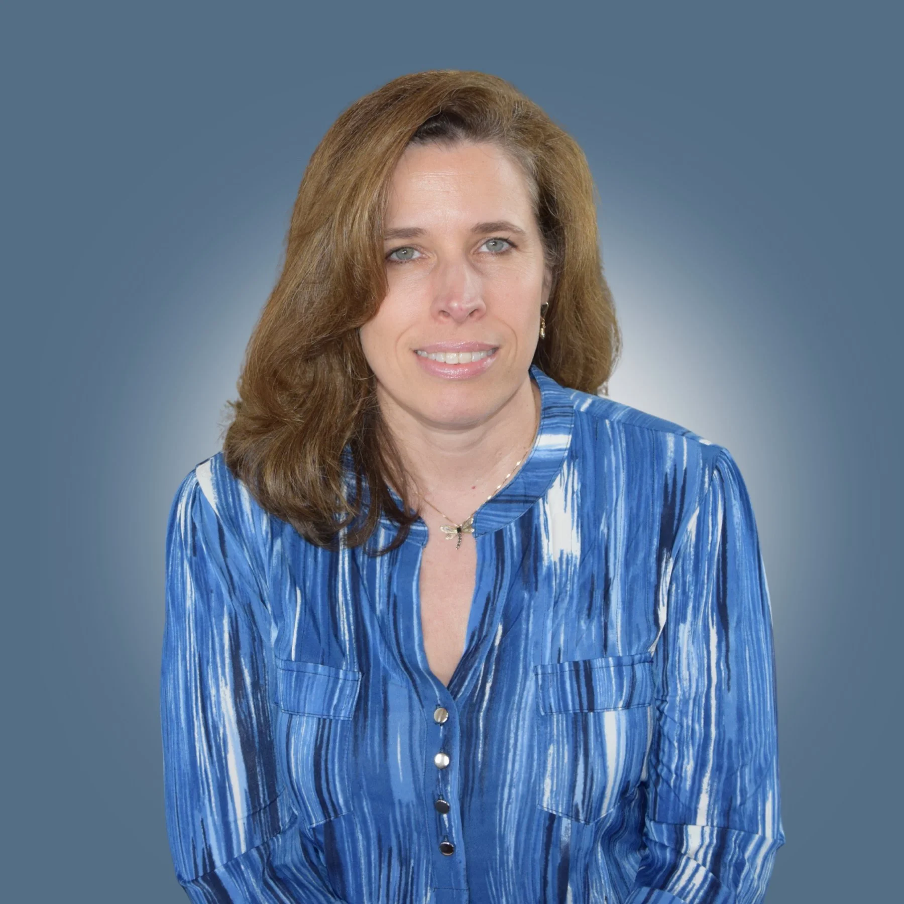 A woman with light brown hair and blue eyes wearing a blue patterned blouse, facing forward with a slight smile, against a blue background.