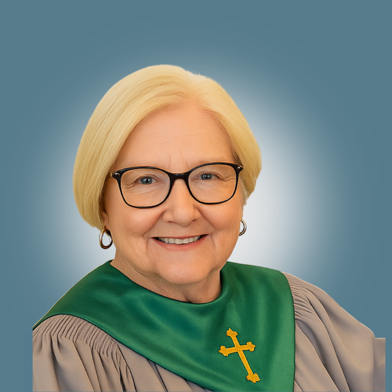 A smiling elderly woman with blonde hair and glasses, wearing a green religious stole with a yellow cross, against a blue background.