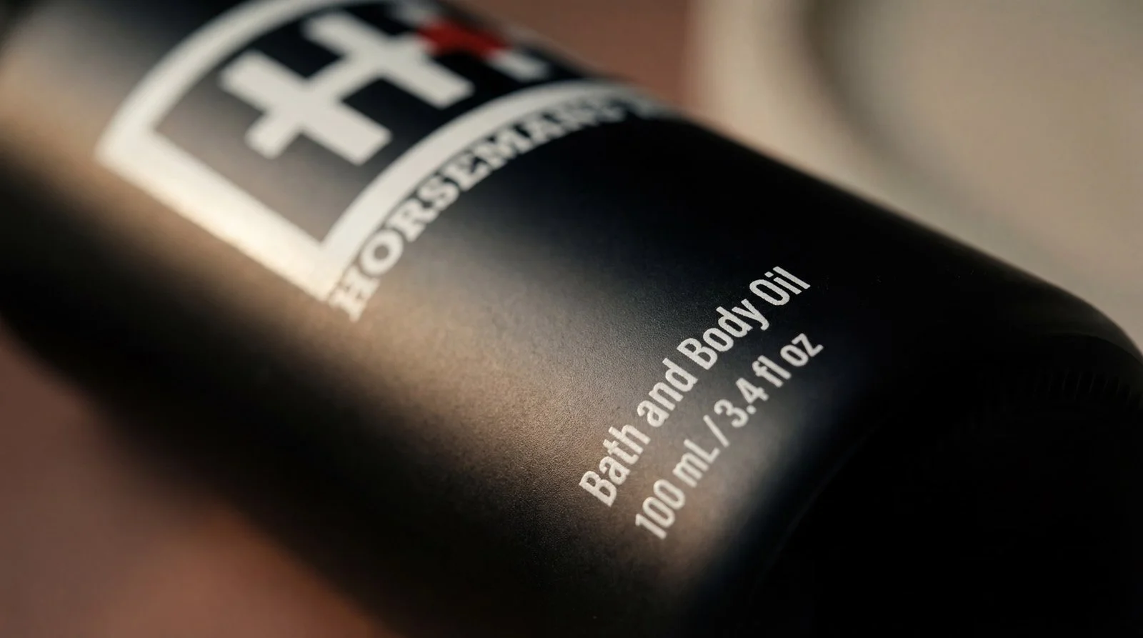 Close-up of a black bottle label with white text reading 'Bath and Body Oil,' indicating a volume of 100 ml or 3.4 fl oz.