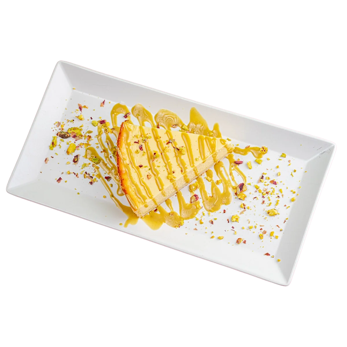 A slice of cheesecake drizzled with caramel sauce, garnished with crushed pistachios on a white rectangular plate.