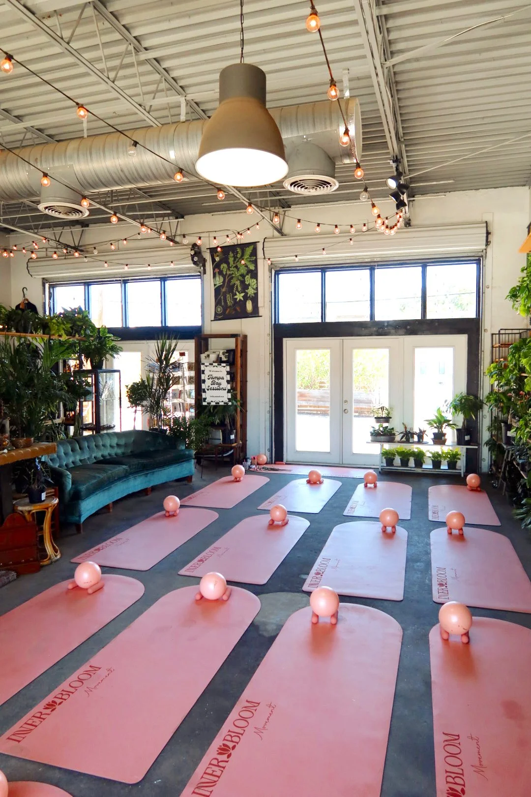 People participating in a yoga class, stretching on mats in a bright, indoor space with large windows showing greenery outside.