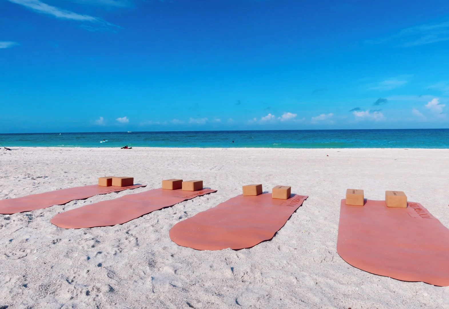 Group of people doing yoga on the sandy beach during sunrise or sunset, with some standing poles and a lifeguard tower in the background.