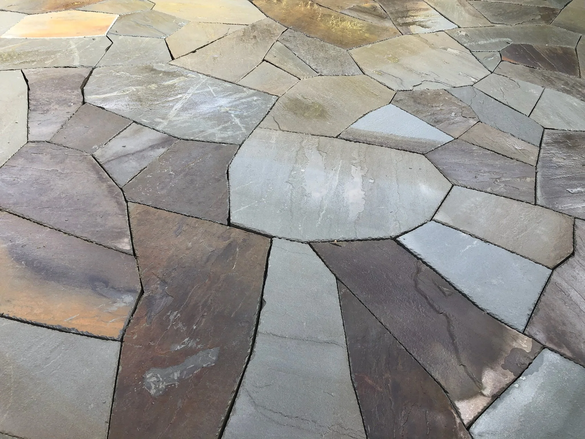 Close-up of irregularly shaped natural stone pavers in shades of gray, beige, and brown forming a textured surface.