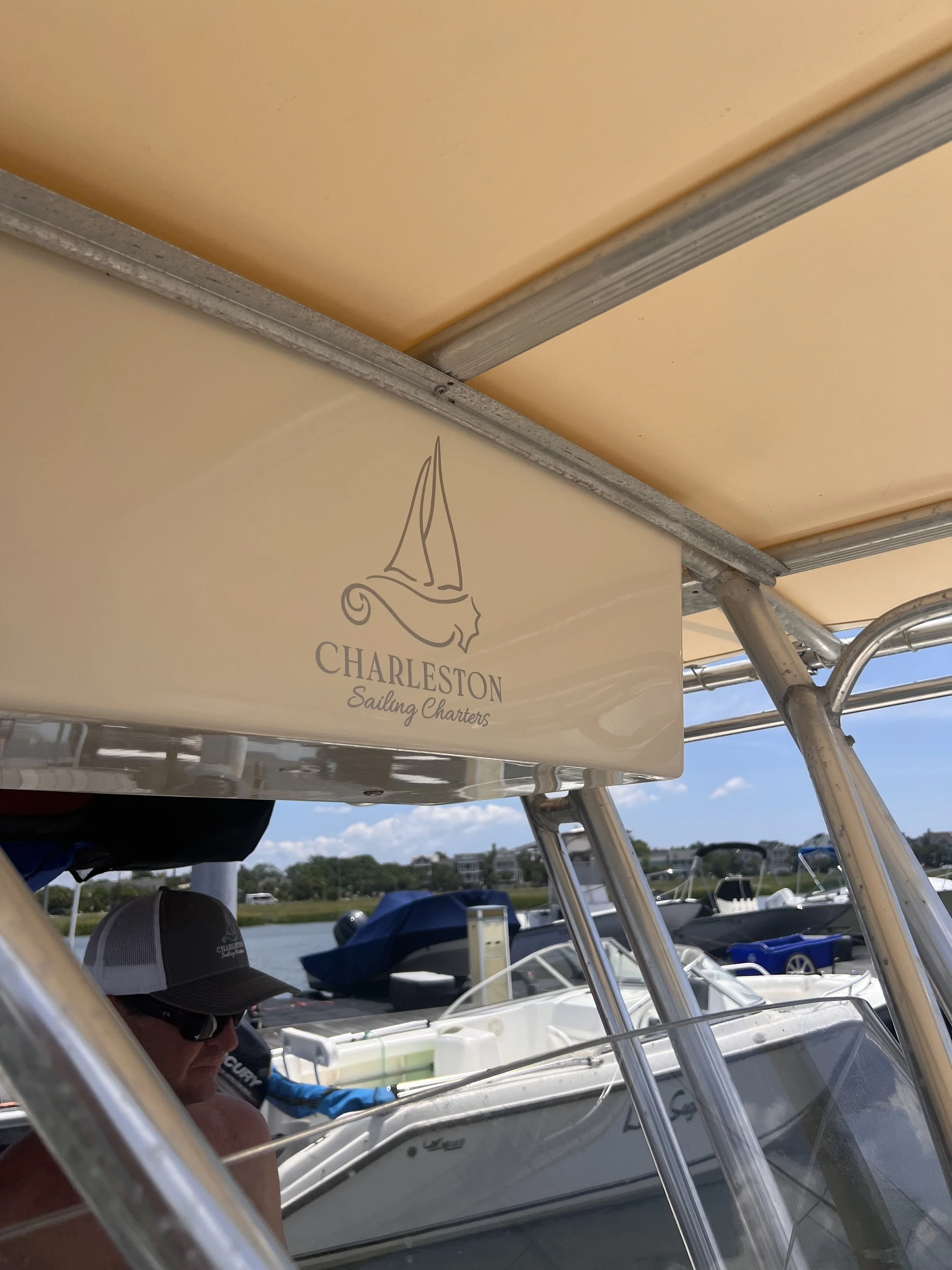 View of a boat with a Charleston Sailing Charters sign, harbor with other boats, in clear weather with blue sky suitable for sailing.