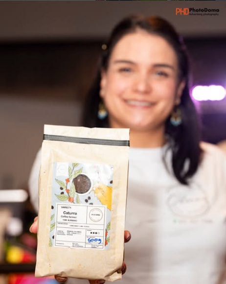 Smiling woman holding a bag of coffee at a coffee shop.