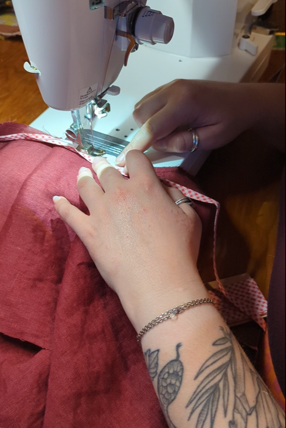 Close up of two hands guiding berry coloured fabric through a sewing machines.