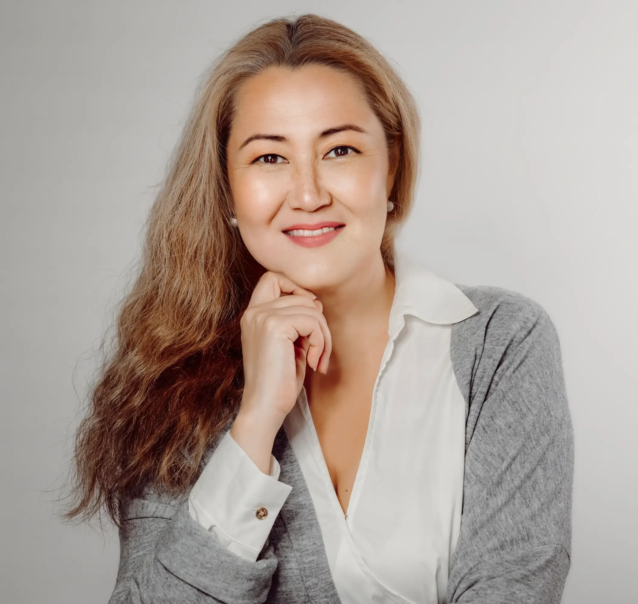 Alla Folsom Headshot: Russian women, therapist, smiling at camera, wearing long-sleeve grey sweater over white blouse, light grey background 