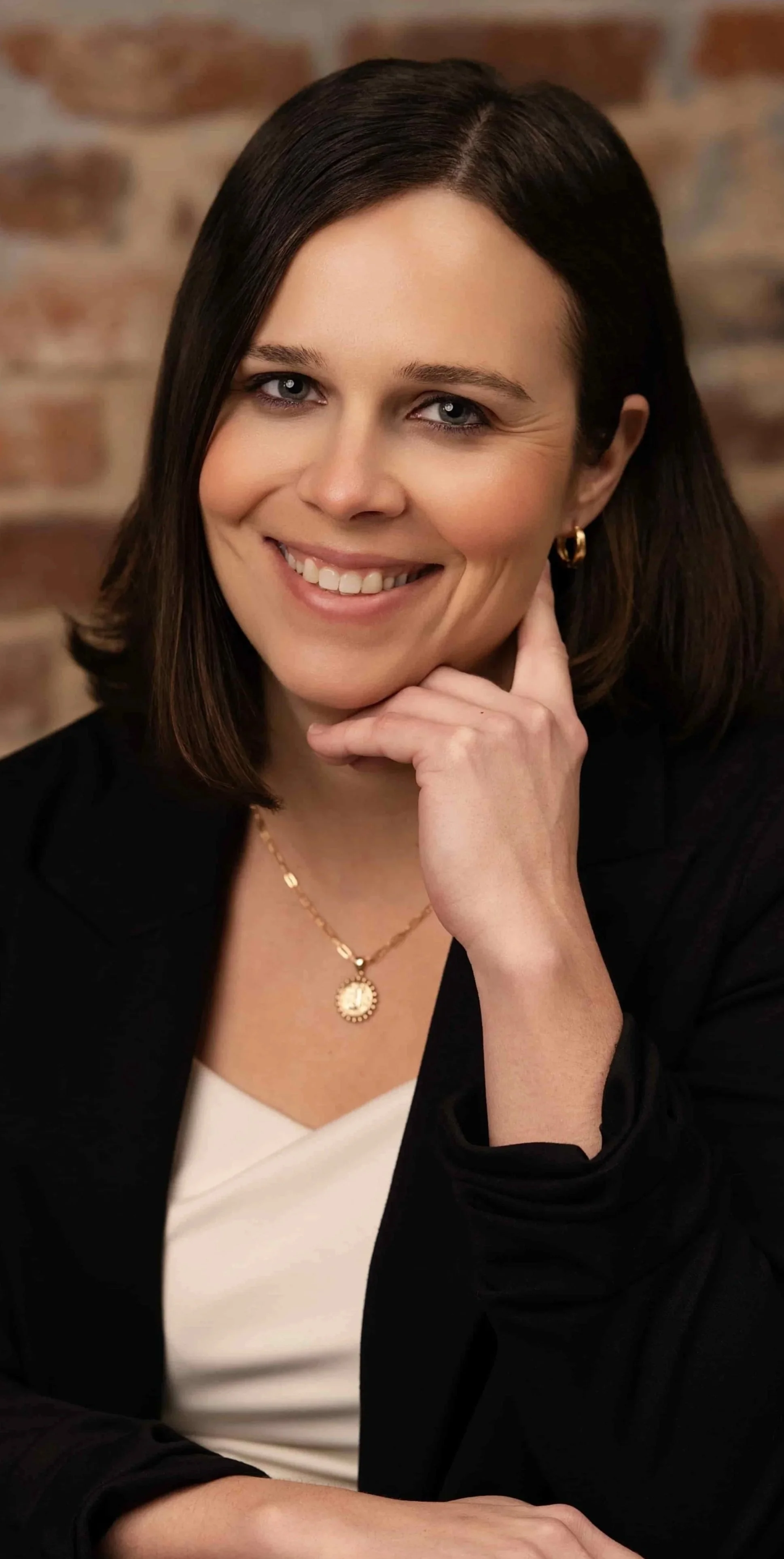 Ericka Jefferson headshot: Female therapist in white shirt with black jacket smiles warmly at the camera against blurred brick wall background