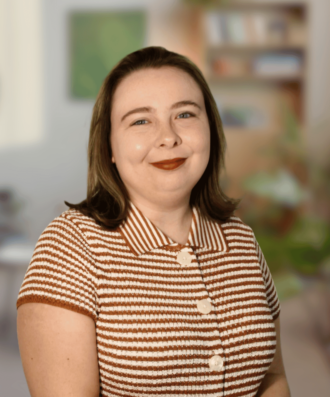 Sara Buchanan: Young white female therapist smiling at the camera, wearing a white and brown striped shirt, in front of blank off white background