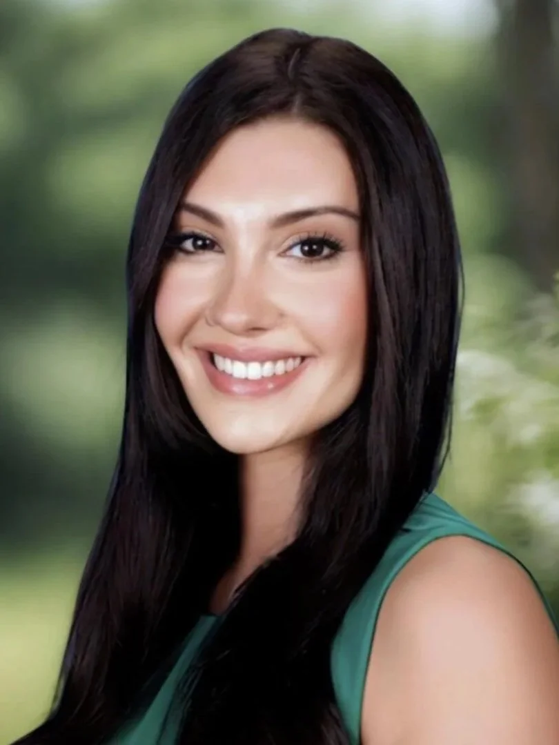 Mackenzie Fezza Headshot: A smiling female therapist with long dark hair and a green sleeveless top outdoors with a blurred green background.