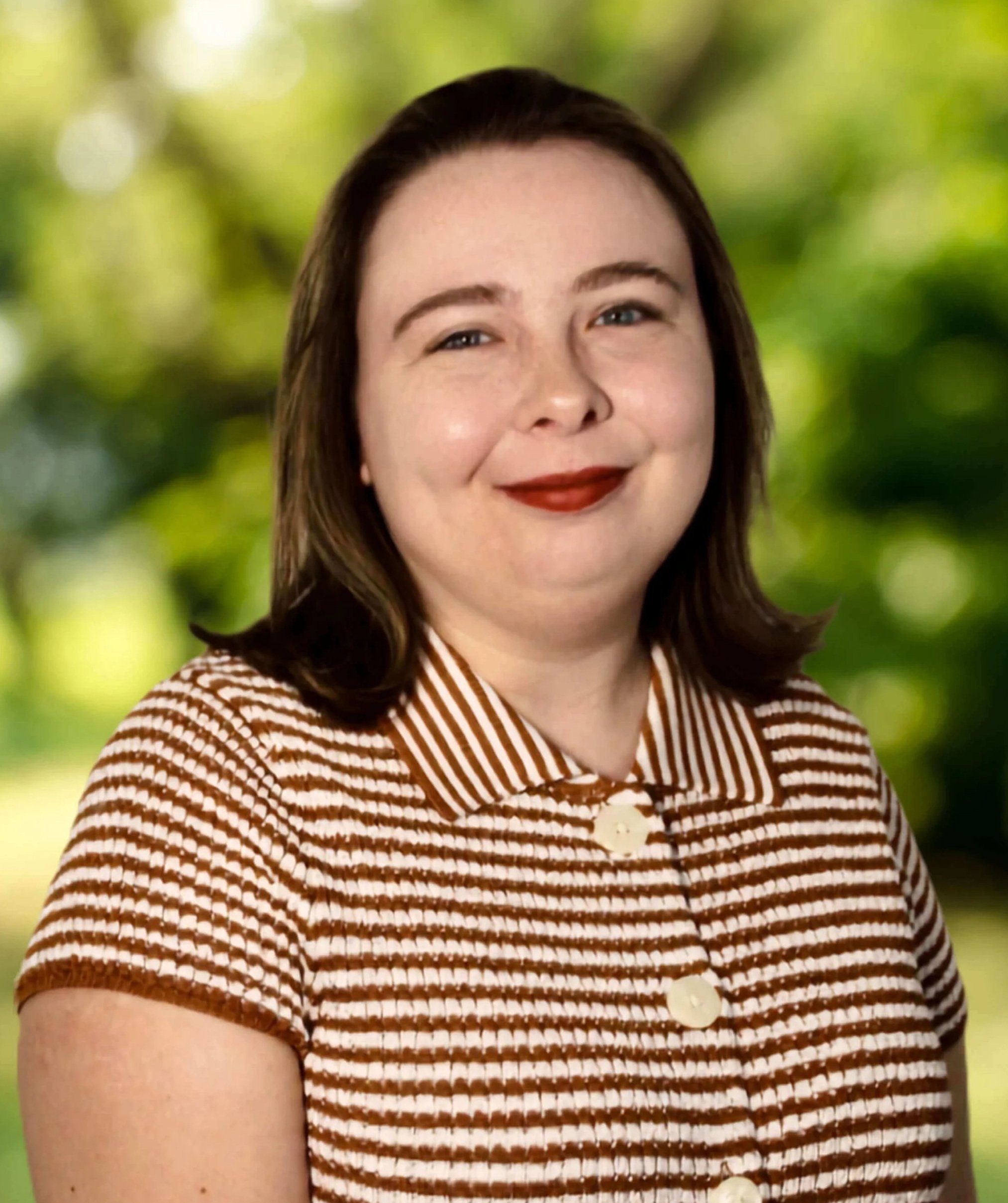 Sara Buchanan: Young white female therapist smiling at the camera, wearing a white and brown striped shirt, in front of blank off white background