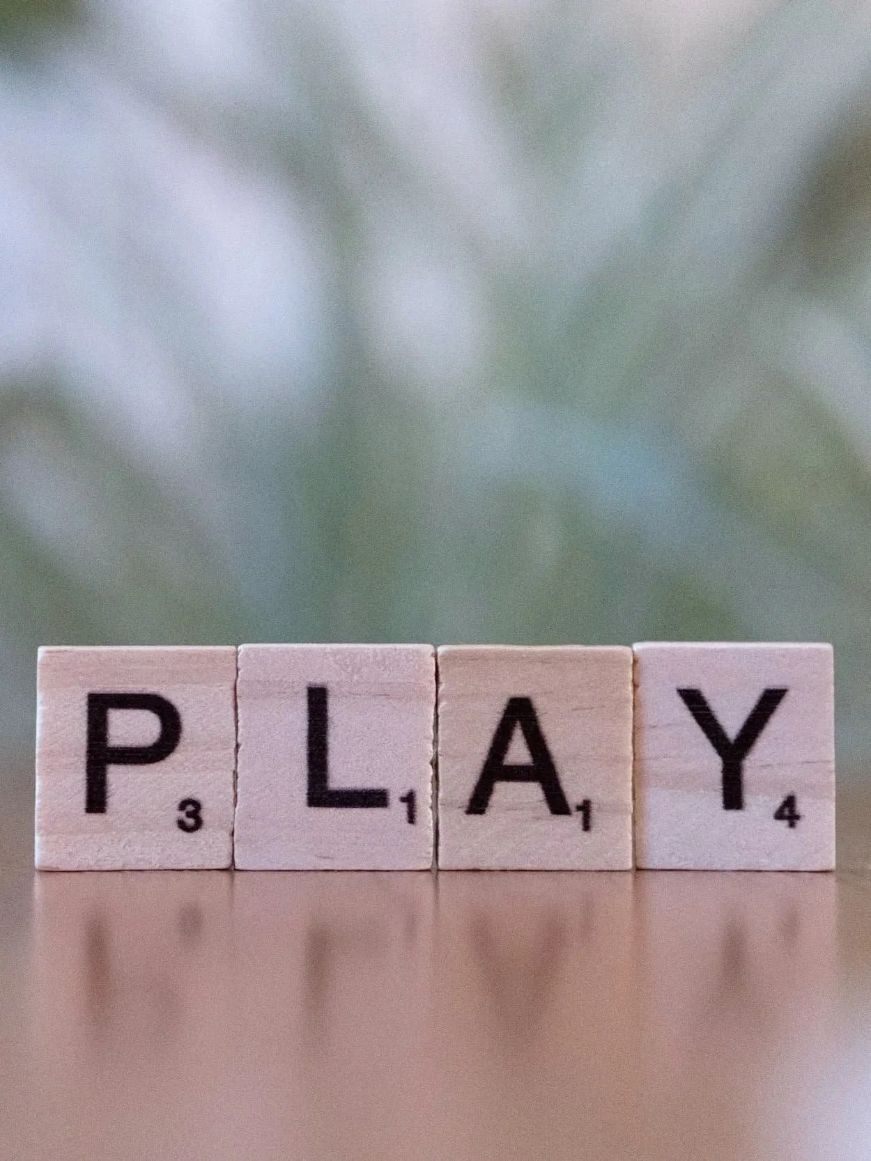 Wooden tiles spelling out 'PLAY' on a reflective surface, with a blurred background.