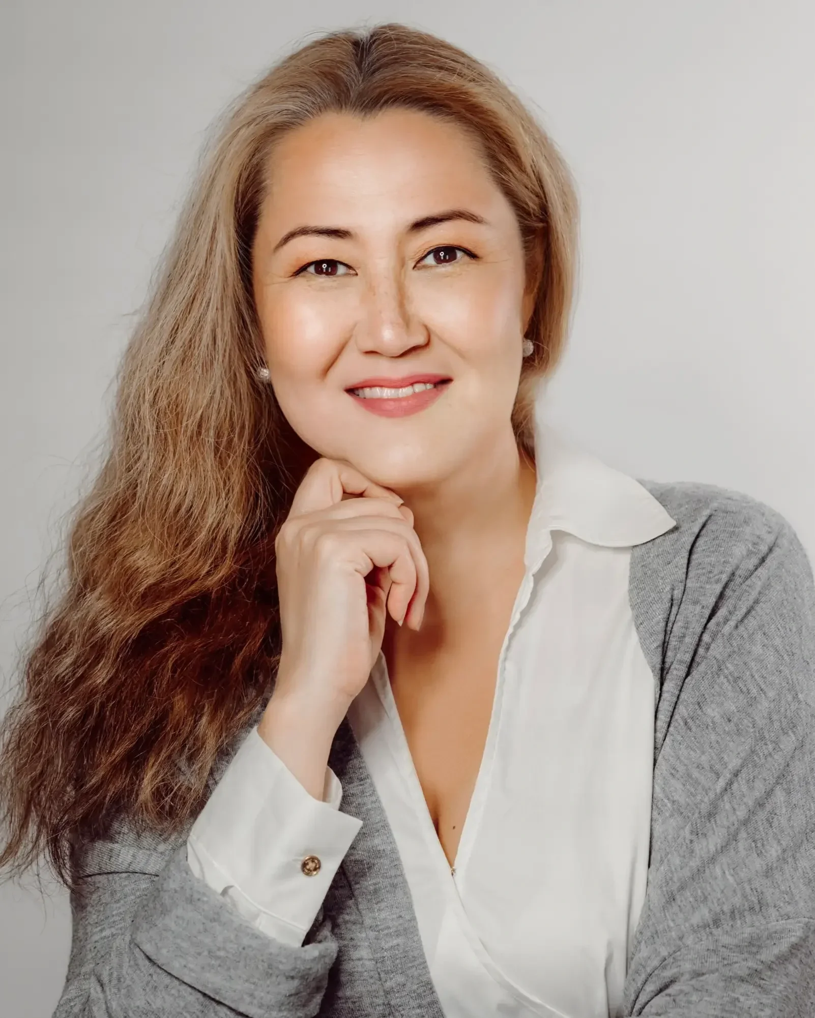 Alla Folsom Headshot: Russian women, therapist, smiling at camera, wearing long-sleeve grey sweater over white blouse, light grey background 