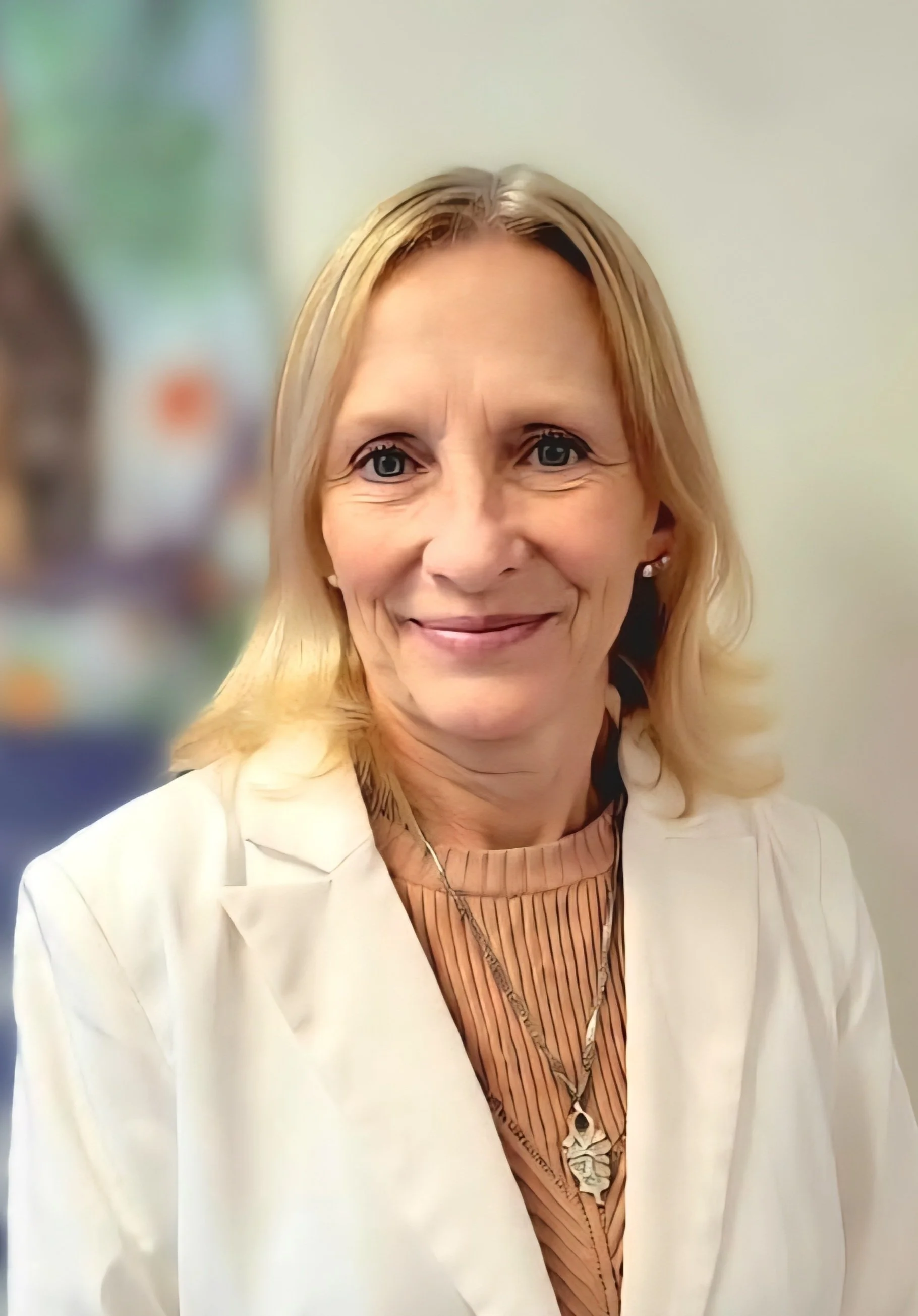 A woman with blonde hair wearing a beige blazer over a pink top, holding a clicker, standing in front of teal curtains.