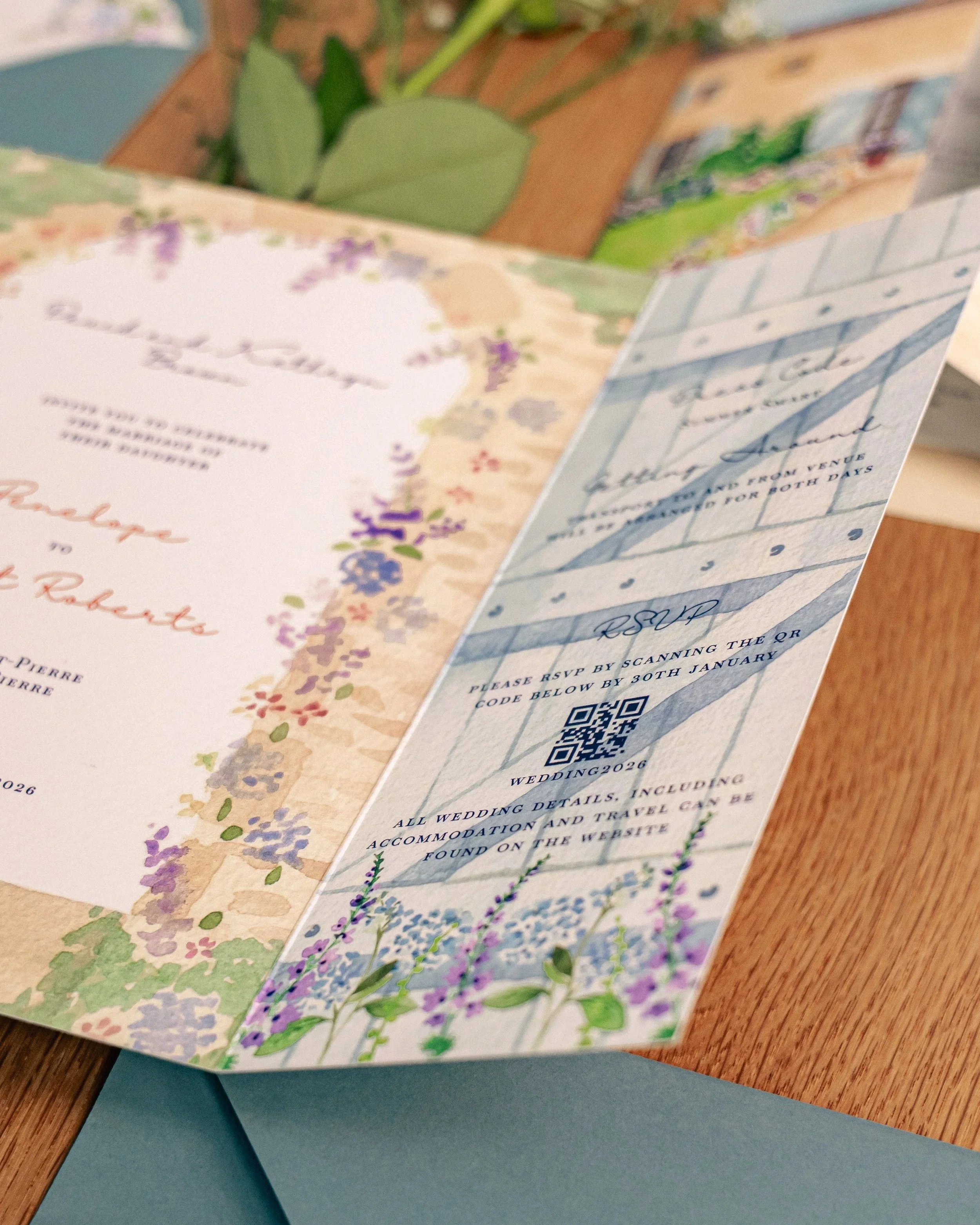 Close-up of wedding invitations with floral designs and RSVP details, placed on a wooden surface.