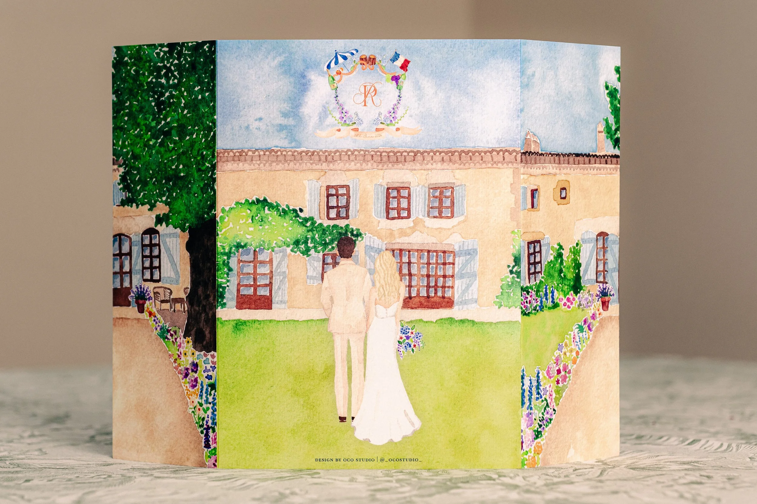 A wedding greeting card with a watercolor illustration of a bride and groom walking towards a mansion, with flowers and greenery surrounding the scene.